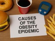 Causes for the Obesity Epidemic Person eating fast food and using a smartphone, symbolizing obesity risk factors. }